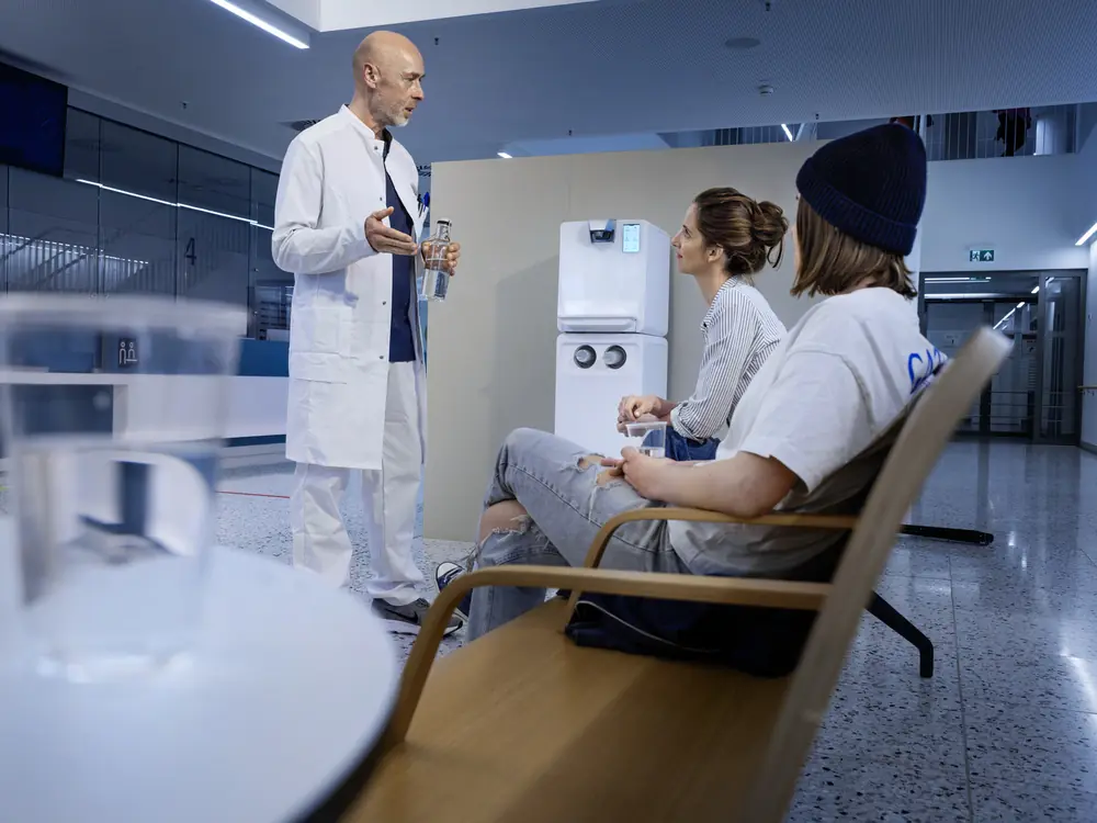 Arzt und Patienten im Wartebereich einer Klinik mit weißem Kärcher Wasserspender