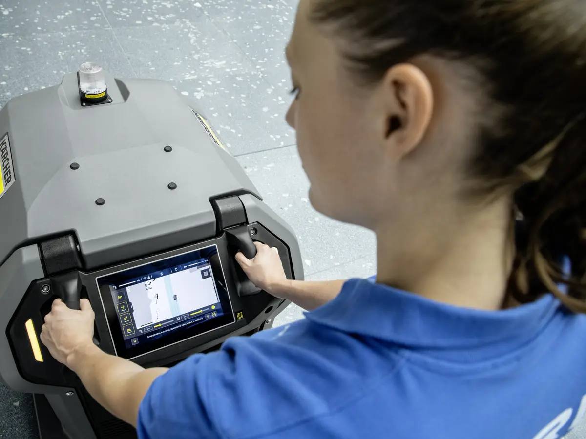 Mitarbeiterin startet am Touchdisplay des KIRA Scheuersaugroboters eine Reinigungsroute