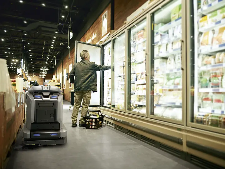 KIRA Scheuersaugroboter im Gang eines Supermarkts vor der Kühltheke
