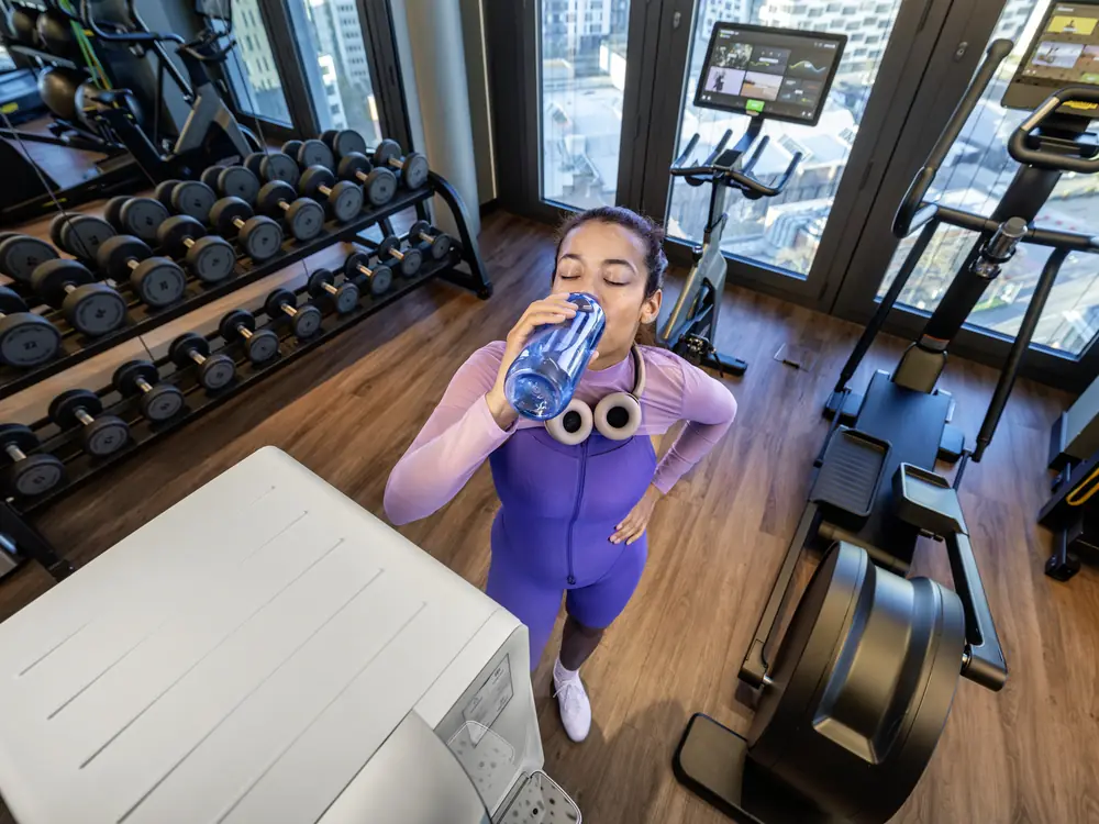 Sportlerin trinkt aus ihrer Trinkflasche im Fitnessraum neben einem Kärcher Wasserspender