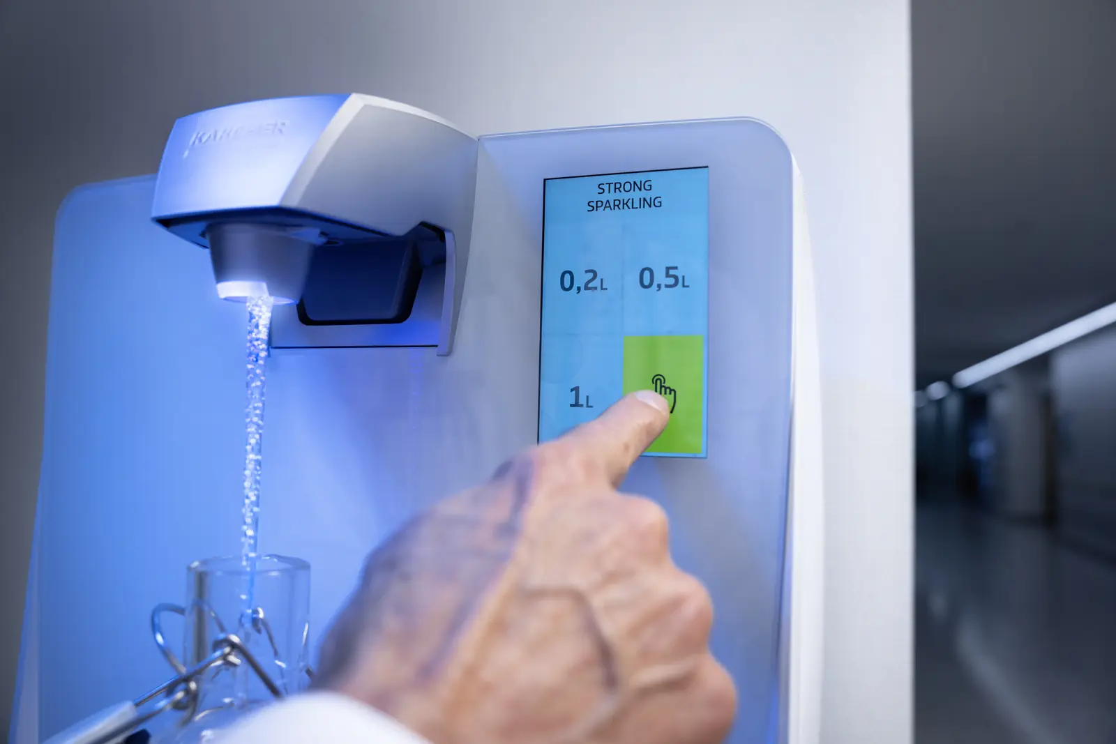 Hand wählt am Touchdisplay stark sprudelndes Wasser, ein Glas wird gefüllt
